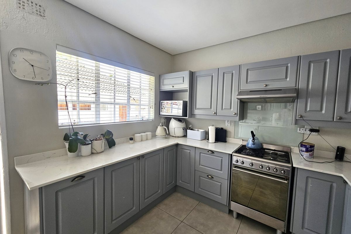 A well-maintained kitchen featuring grey shaker-style cabinetry, stone countertops, a gas stove with an extractor fan, and modern tiled flooring.