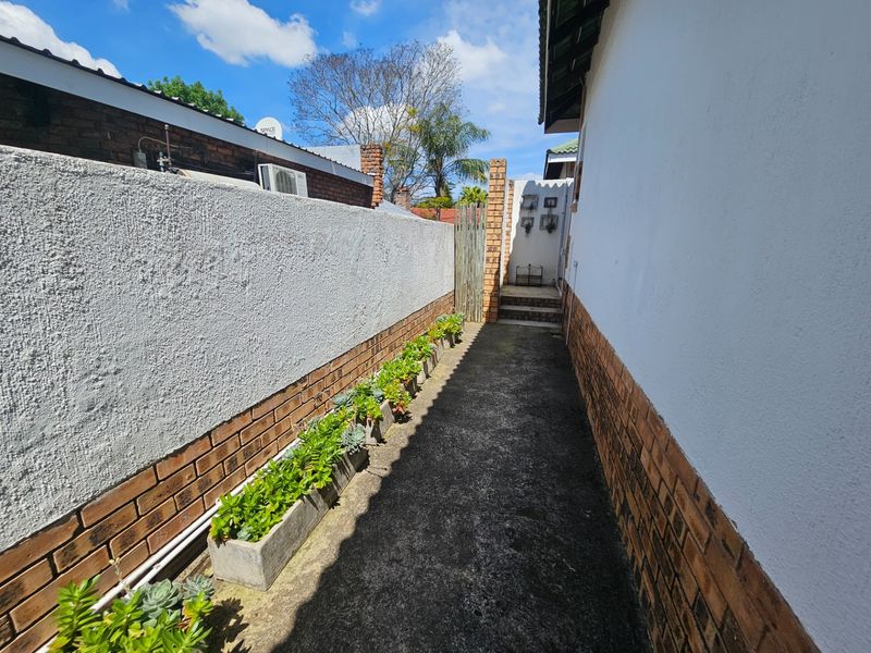 A narrow side passage featuring a concrete walkway, brick boundary walls, and exterior building facade.