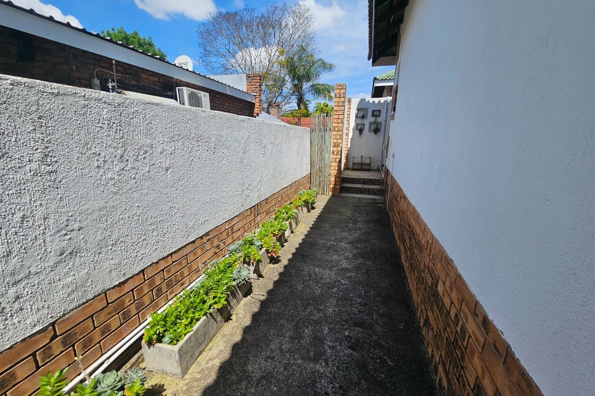 A narrow side passage featuring a concrete walkway, brick boundary walls, and exterior building facade.