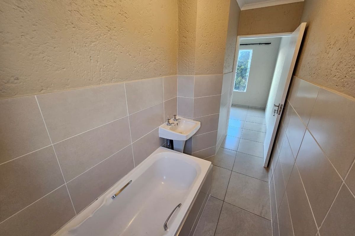 A functional bathroom featuring a bathtub, pedestal basin, and neutral wall and floor tiling, offering a clean and simple layout.