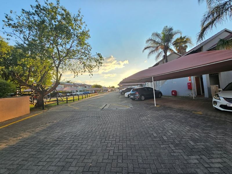 Exterior view of the townhouse complex featuring a paved driveway, covered parking bays, and established landscaping.