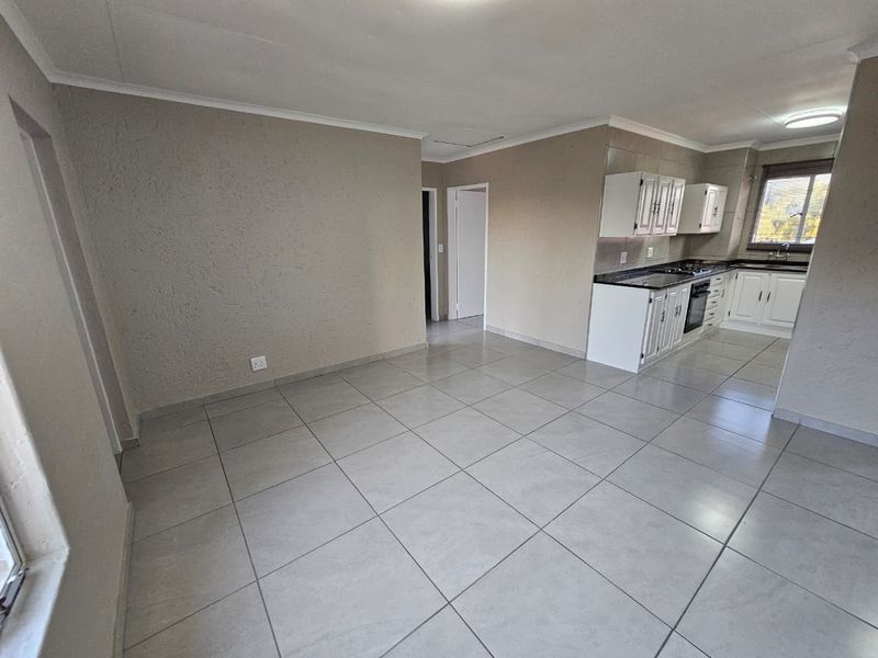 An open-plan living and kitchen area featuring neutral tiled flooring, coved ceilings, and functional built-in kitchen cabinetry with integrated appliances.