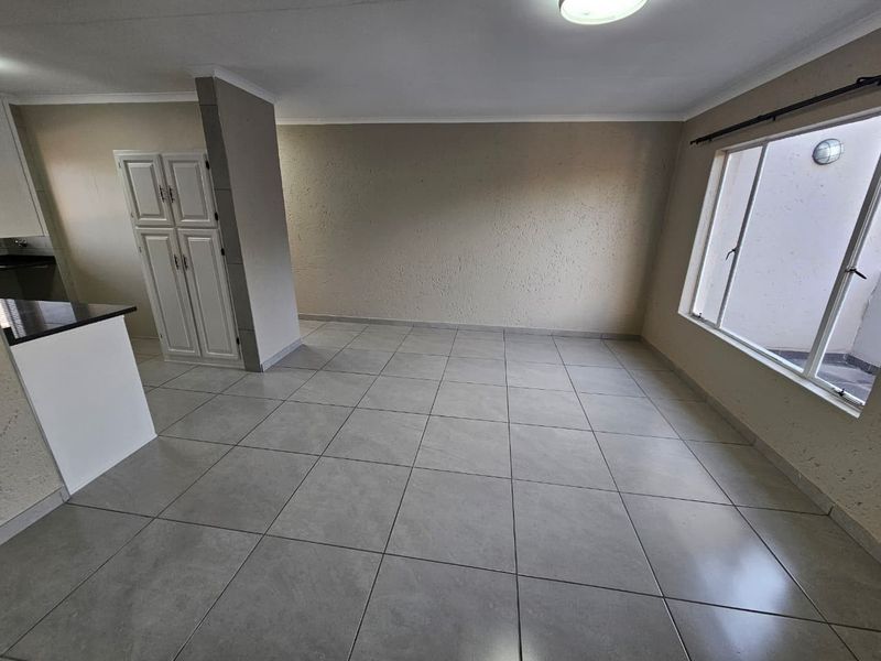 Spacious open-plan living area featuring neutral tiled flooring, built-in cabinetry, and large windows providing ample natural light.