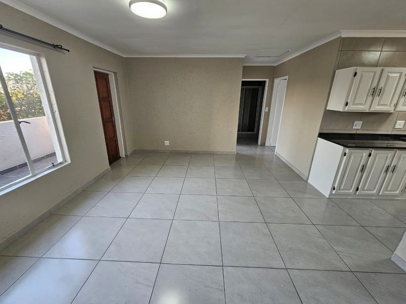 An open-plan living and kitchen area featuring neutral tiled flooring, built-in cabinetry with granite countertops, and direct access to an outdoor balcony.