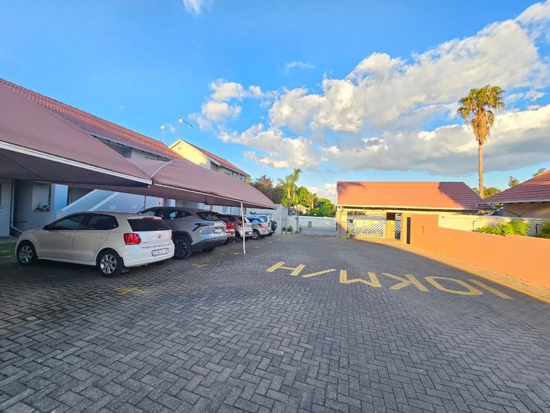 Exterior view of the townhouse complex featuring a paved driveway, covered parking bays, and secure perimeter walling.