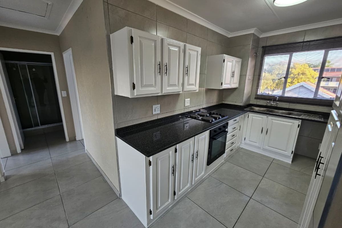 A clean, functional kitchen featuring white cabinetry, dark granite countertops, built-in oven, gas hob, and tiled finishes throughout.