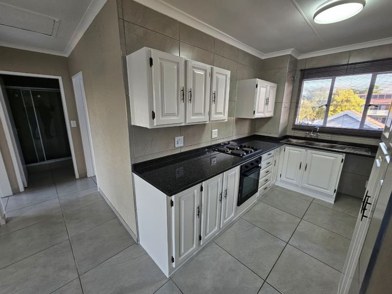 A clean, functional kitchen featuring white cabinetry, dark granite countertops, built-in oven, gas hob, and tiled finishes throughout.