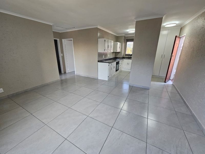 Spacious open-plan living area featuring large format floor tiles, neutral wall tones, and a functional kitchen with built-in cabinetry and appliances.