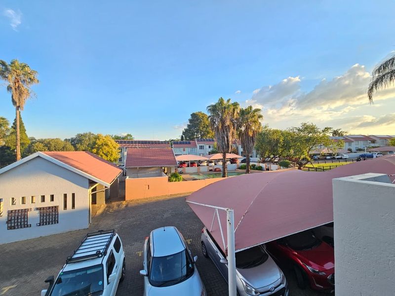 An elevated view of the townhouse complex parking area featuring shade cloth carports, paved driveway, and communal swimming pool in the background.