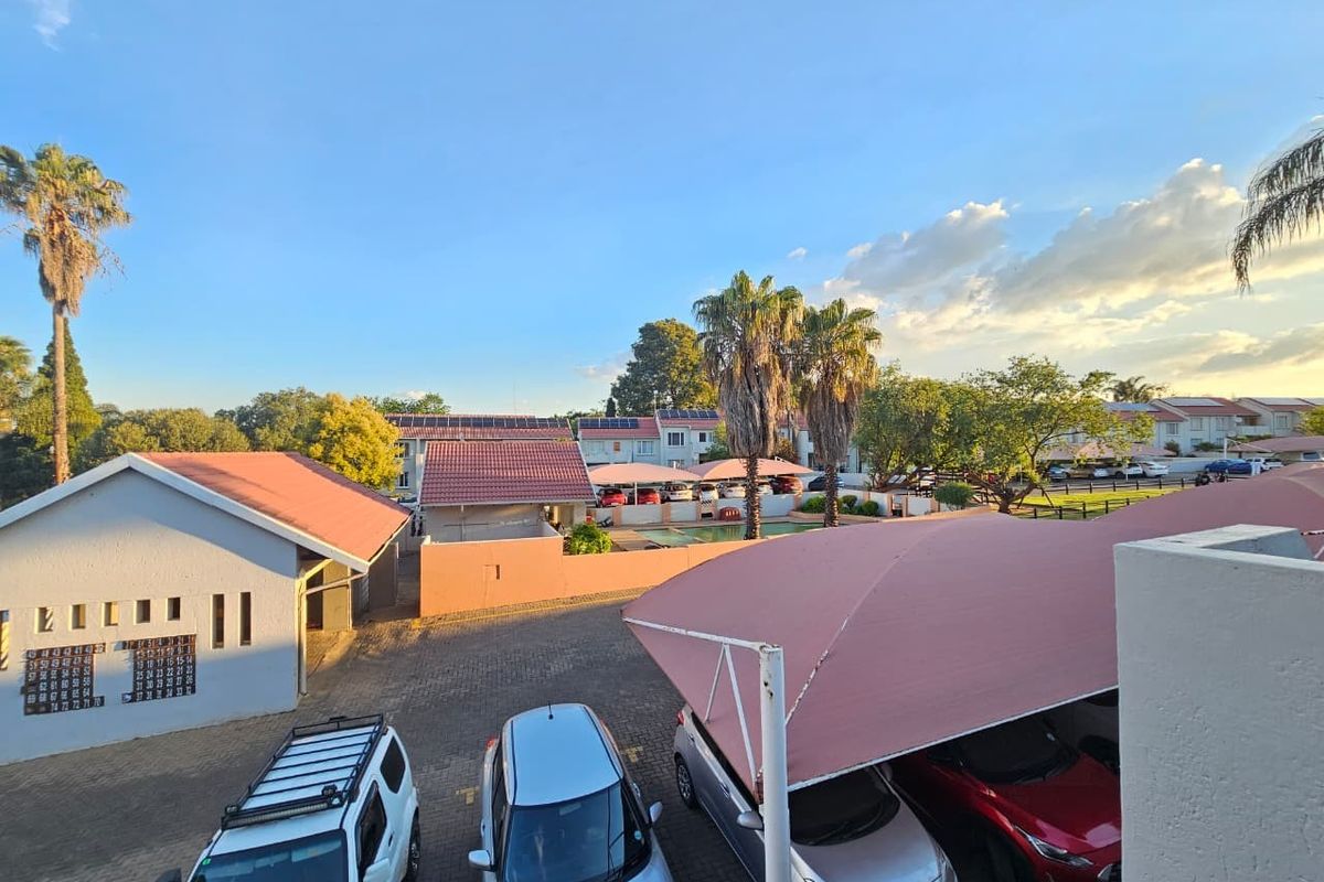 An elevated view of the townhouse complex parking area featuring shade cloth carports, paved driveway, and communal swimming pool in the background.