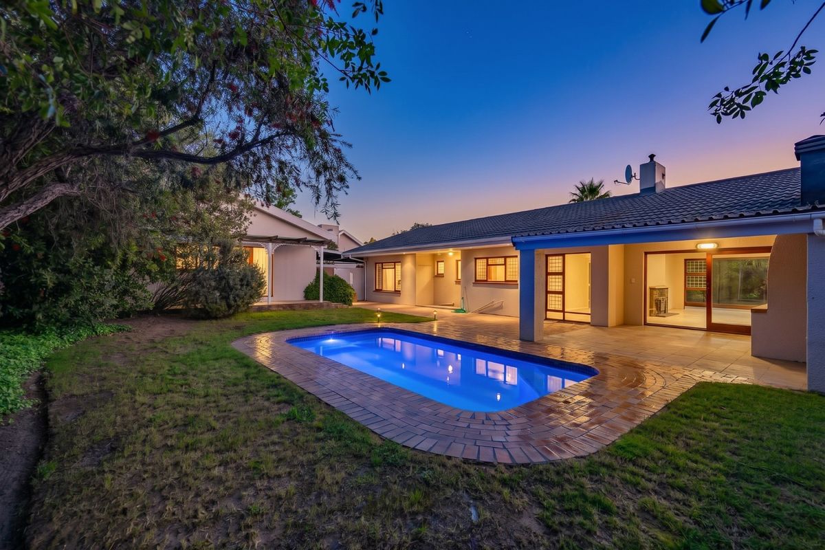A well-maintained rear exterior view featuring a swimming pool, paved patio area, and direct access to the home through sliding doors at twilight.