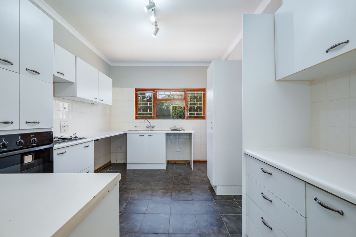 A functional kitchen featuring white built-in cabinetry, laminate countertops, a built-in oven, hob, and tiled flooring with a window providing natural light.