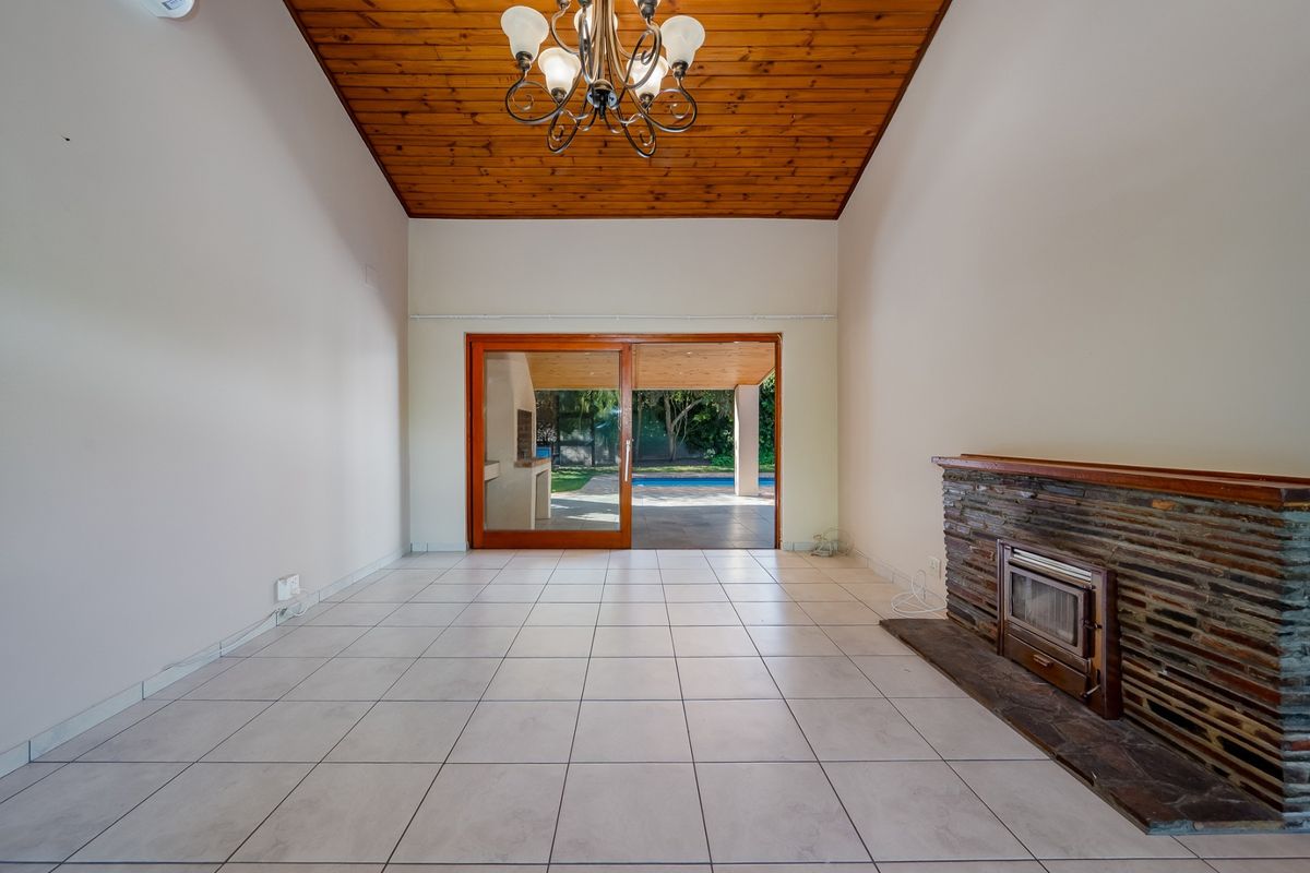 Spacious living room featuring a vaulted timber ceiling, stone-clad fireplace with a built-in stove, and large sliding doors opening to the patio and pool area.