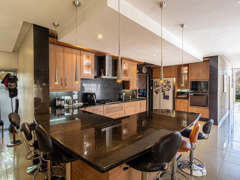 Modern kitchen featuring extensive wooden cabinetry, granite countertops, a large breakfast island, and integrated appliances under a stylish drop ceiling.