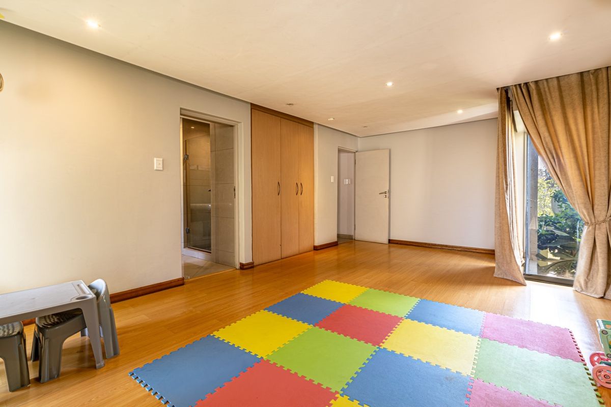 Spacious bedroom featuring laminate flooring, built-in cupboards, recessed lighting, and direct access to an en-suite bathroom and outdoor area via a sliding glass door.