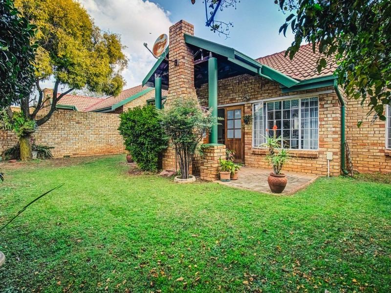 Rear view of a face brick house featuring a paved patio area, tiled roof, and established garden surroundings.