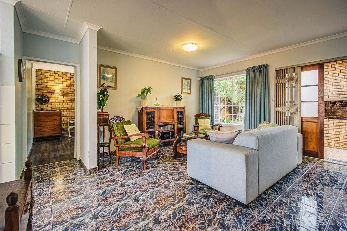 A living room featuring tiled flooring, coving, and a sliding security gate leading to an outdoor area with exposed brickwork.
