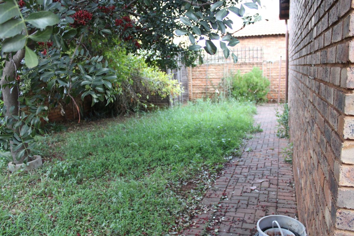 A side garden area featuring brick paving and a perimeter boundary wall, currently requiring landscaping and maintenance.