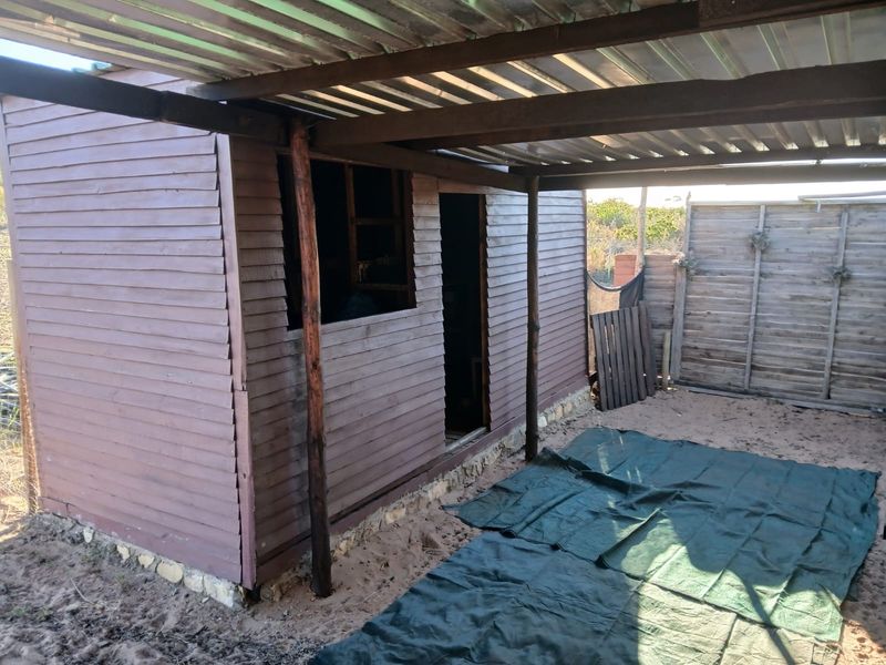 A basic timber-clad structure with a corrugated metal roof and attached outdoor area, showing signs of significant weathering and wear.
