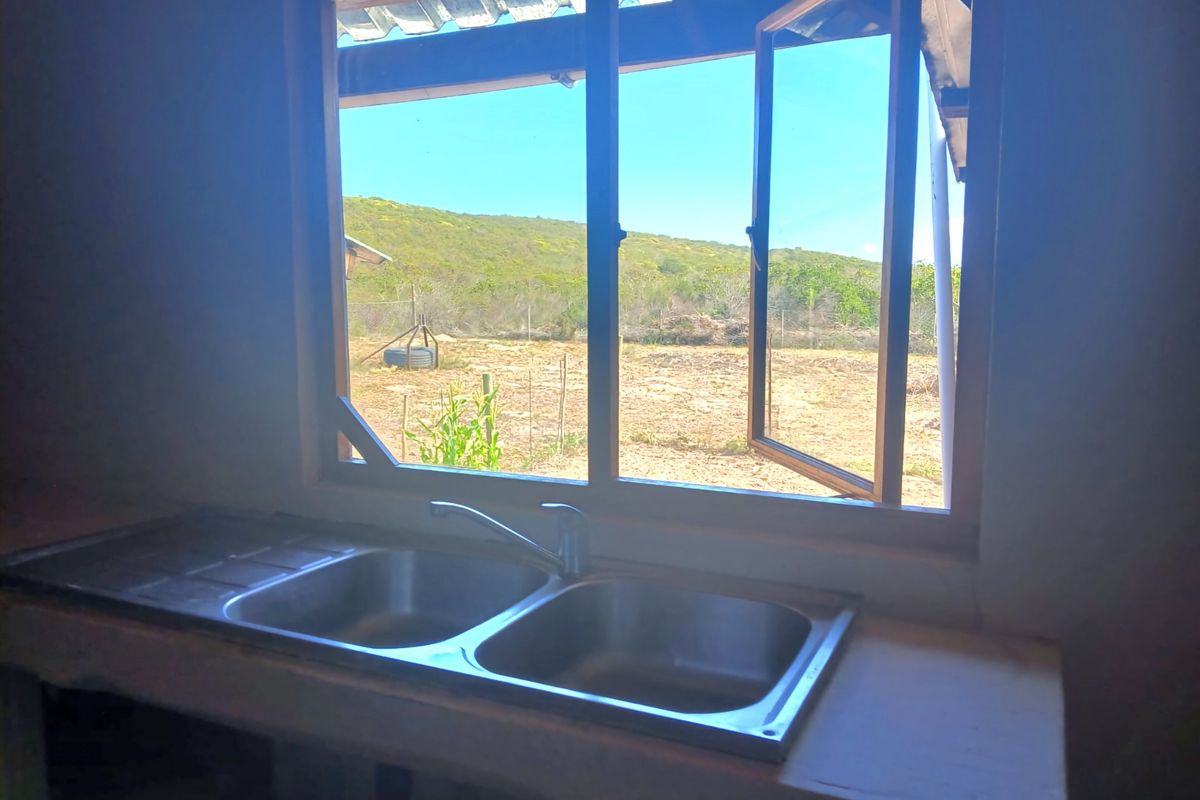 A basic kitchen area featuring a double bowl stainless steel sink and concrete countertop, overlooking a rural landscape through an open casement window.
