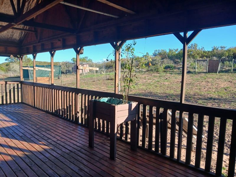 A spacious covered timber deck featuring exposed rafters and a wooden balustrade, overlooking an expansive rural garden area.