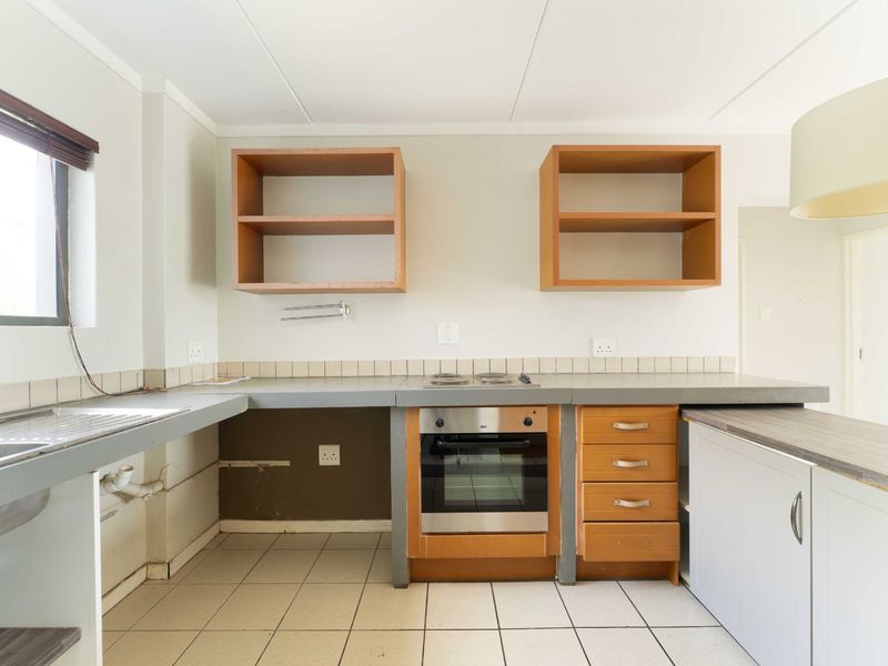 A functional kitchen space featuring built-in oven, hob, and sink, with open shelving and base cabinetry, ready for renovation or modern updates.