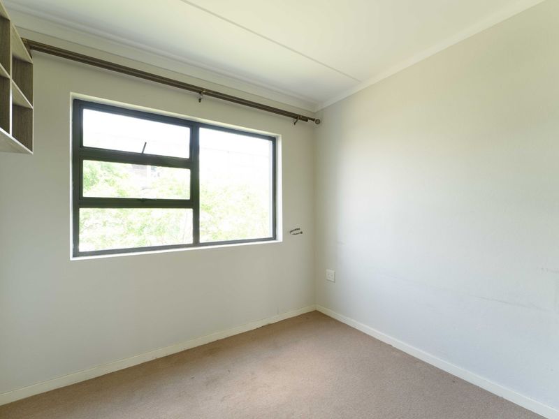 A vacant bedroom featuring neutral walls, carpet flooring, built-in shelving, and a large window with a curtain rod.
