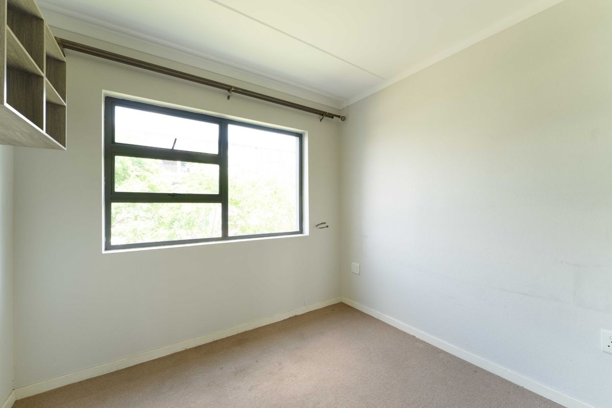 A vacant bedroom featuring neutral walls, carpet flooring, built-in shelving, and a large window with a curtain rod.