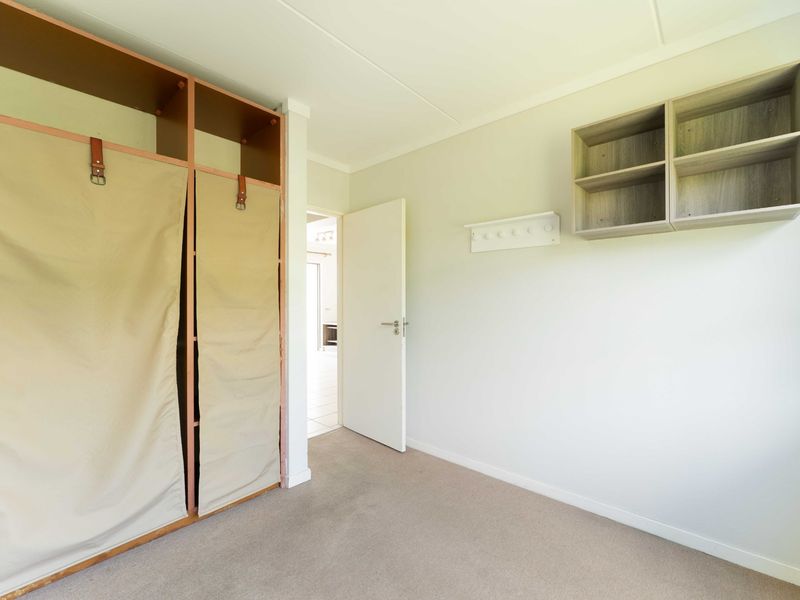 A clean, empty bedroom featuring neutral carpet flooring, a built-in wardrobe with fabric covers, and wall-mounted storage shelving.