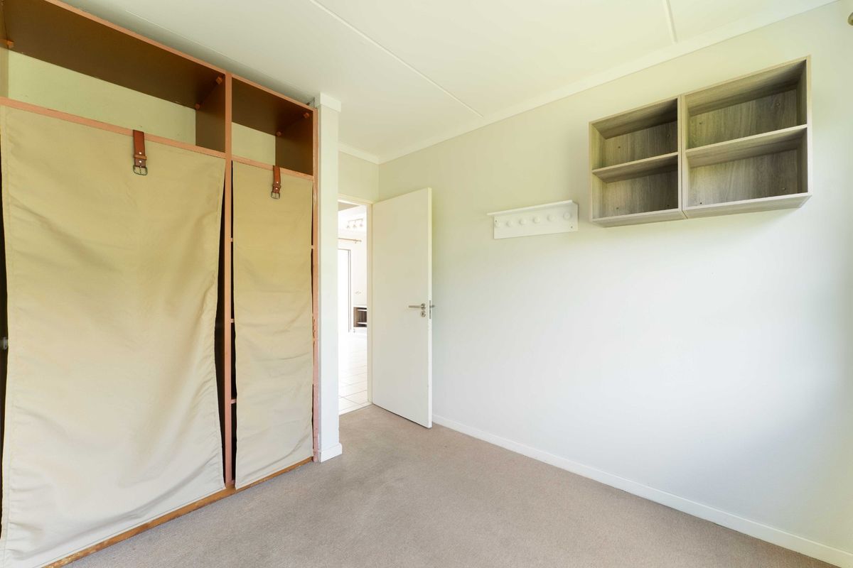 A clean, empty bedroom featuring neutral carpet flooring, a built-in wardrobe with fabric covers, and wall-mounted storage shelving.