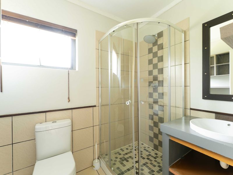 A functional bathroom featuring a corner shower enclosure, a modern vanity basin, and a toilet, finished with neutral wall and floor tiling.