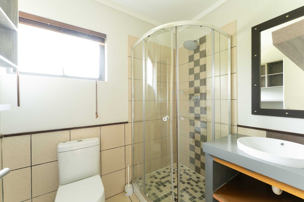 A functional bathroom featuring a corner shower enclosure, a modern vanity basin, and a toilet, finished with neutral wall and floor tiling.
