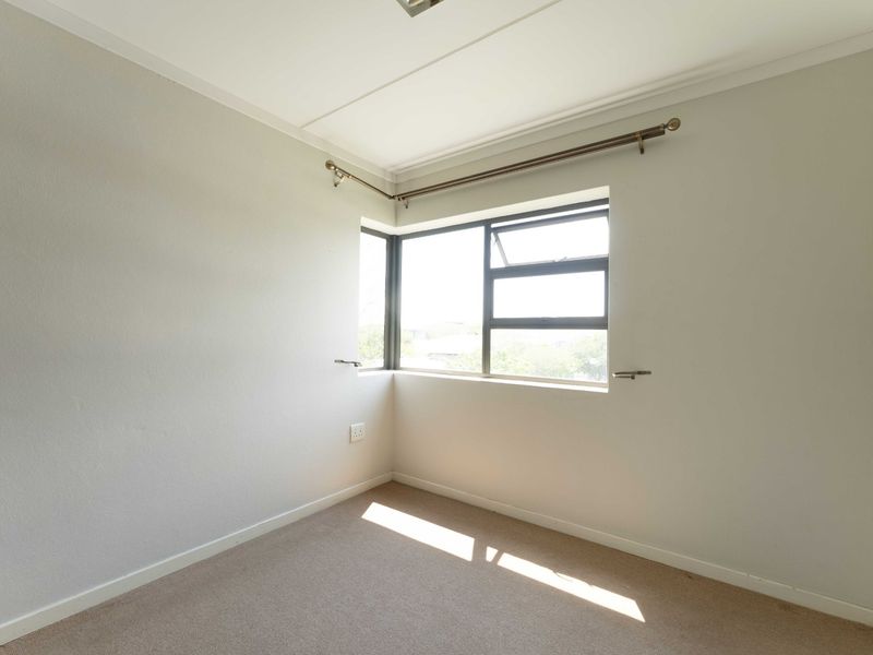 A bright, empty bedroom featuring neutral walls, carpeted flooring, and a corner window with an installed curtain rod.