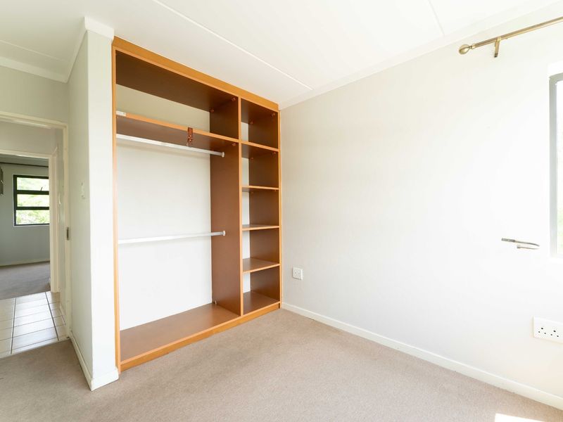 A bright, empty bedroom featuring a built-in wooden wardrobe, neutral carpeted flooring, and clean white walls, offering a versatile space for customization.