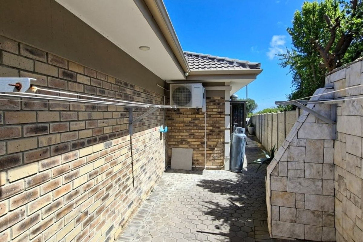 A side exterior walkway featuring brick and stone cladding, paved flooring, and a wall-mounted air conditioning unit.