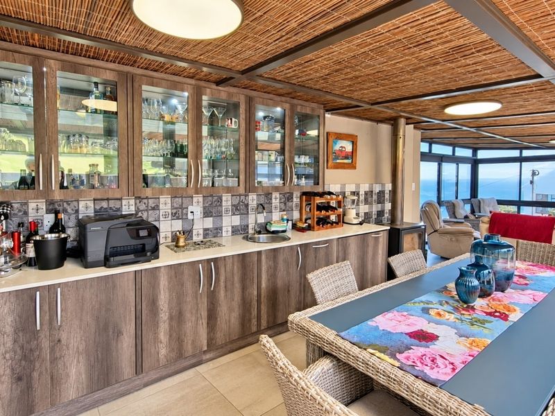 Open-plan living and dining area featuring built-in cabinetry, a tiled backsplash, a wood-burning fireplace, and expansive glass doors with ocean views.