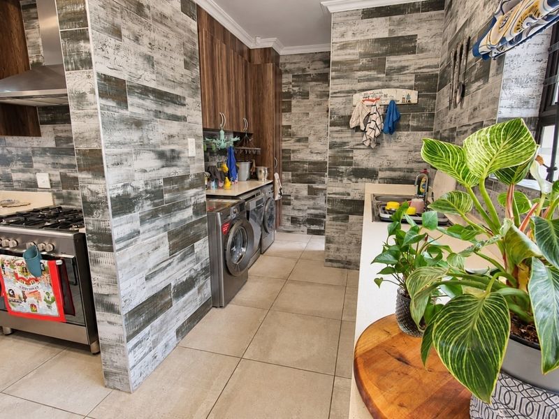 Modern kitchen featuring wood-look cabinetry, stone countertops, gas stove with extractor, and distinctive textured wall tiling with integrated laundry appliances.