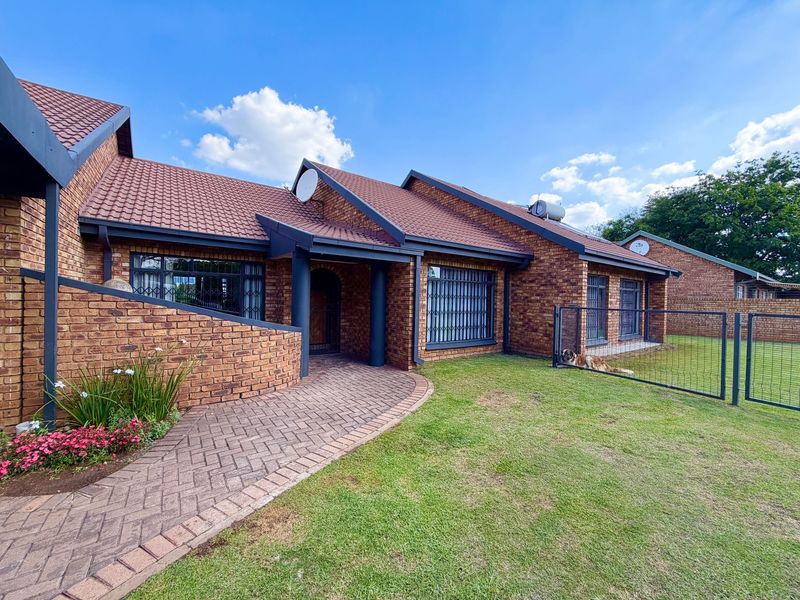 A well-maintained face brick home featuring a tiled roof, paved entrance walkway, and secure metal fencing, set within a neat garden environment.