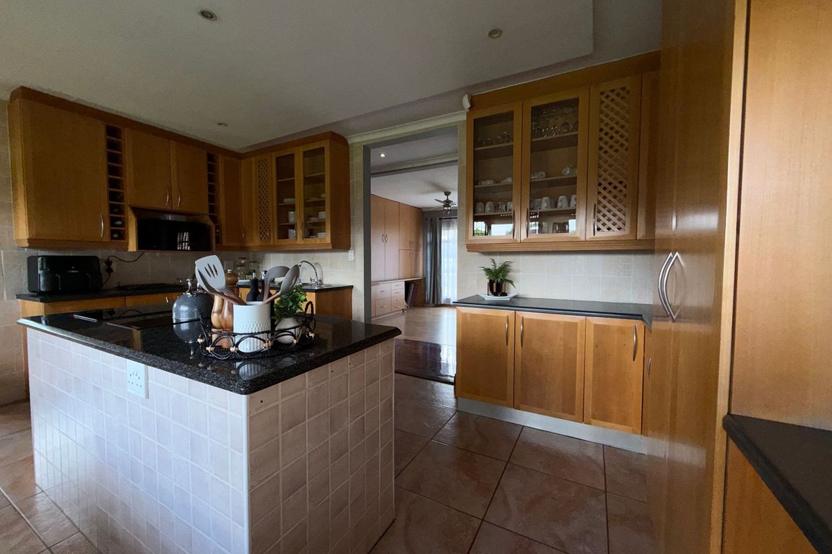 A functional kitchen featuring wooden cabinetry, granite countertops, a tiled island, and tiled flooring, with an open transition to an adjacent living area.
