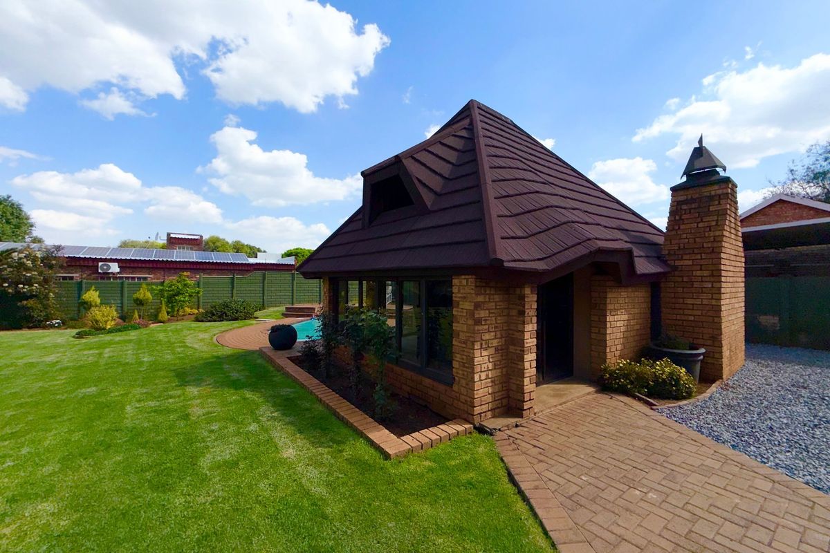 A well-maintained rear garden featuring a brick outbuilding with a chimney, a paved walkway, and a swimming pool set within a landscaped lawn.