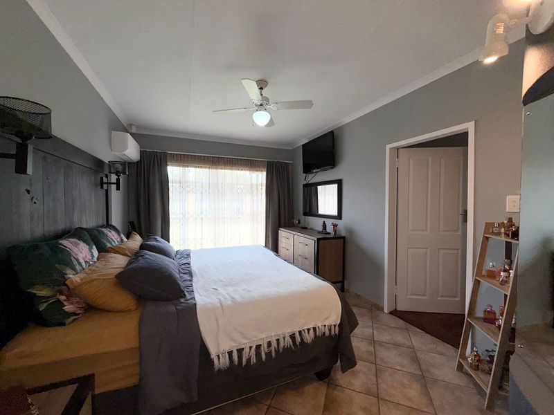 A well-maintained bedroom featuring tiled flooring, a ceiling fan, and a split-system air conditioner, offering a comfortable and functional living space.