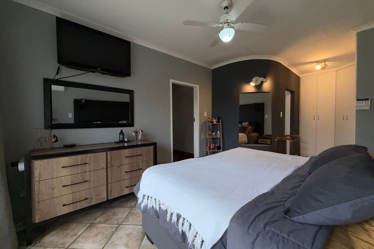 A spacious bedroom featuring tiled flooring, built-in cupboards, and a ceiling fan, with a neutral grey color scheme.