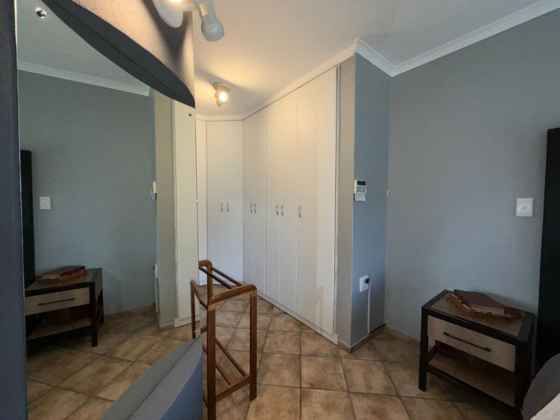 Bedroom featuring built-in white cupboards, tiled flooring, and a security alarm keypad.