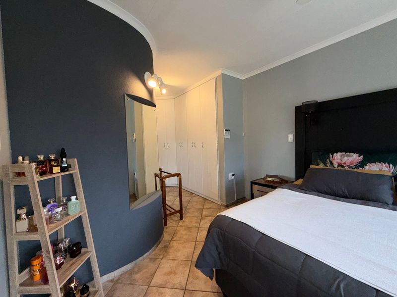 A well-maintained bedroom featuring a curved accent wall, built-in cupboards, and tiled flooring, offering a functional and comfortable living space.