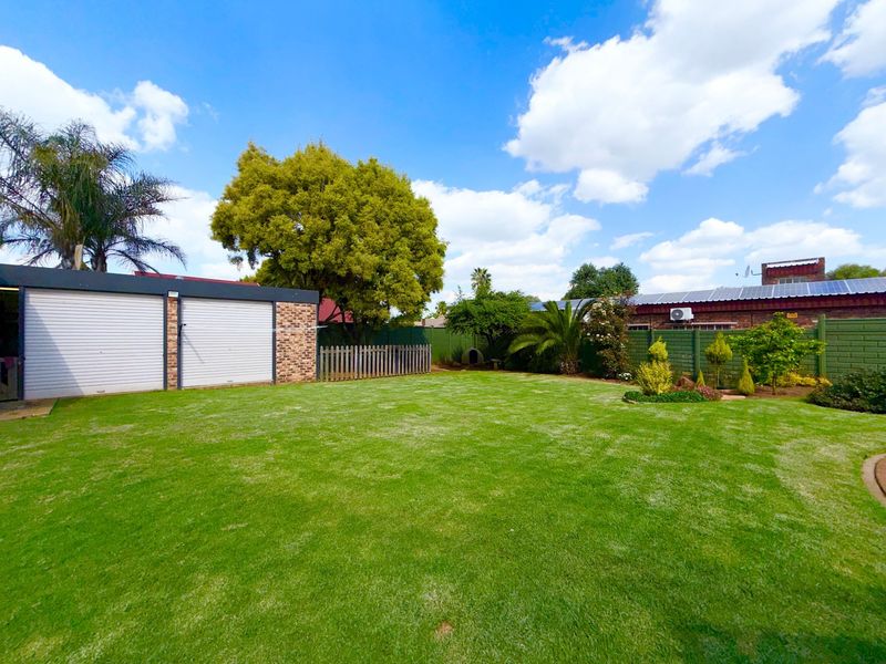 A spacious, well-maintained backyard featuring a large lawn, perimeter fencing, and a double garage with roller doors.