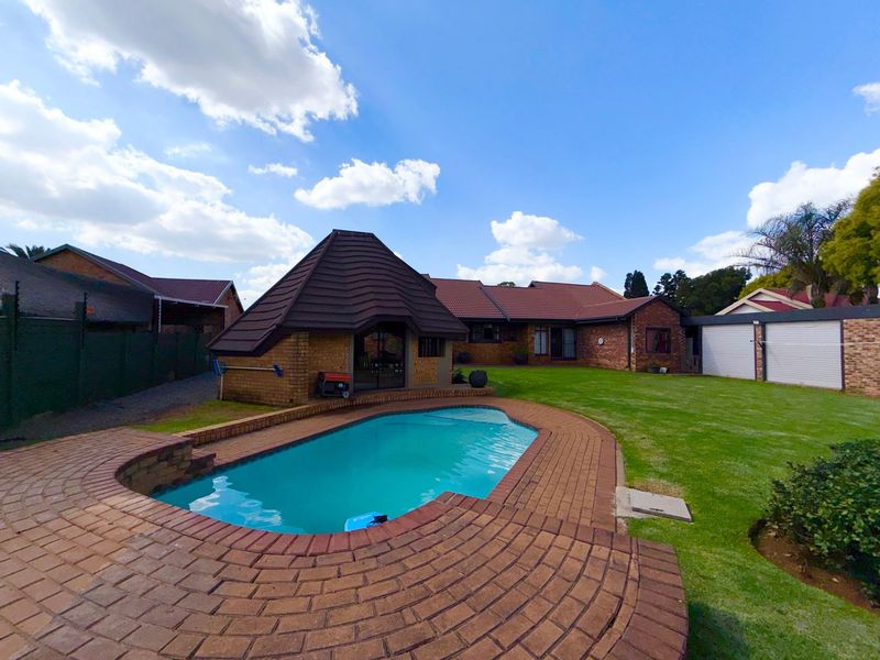 Spacious backyard featuring a swimming pool with brick surround, a thatched lapa, and a well-maintained lawn area.