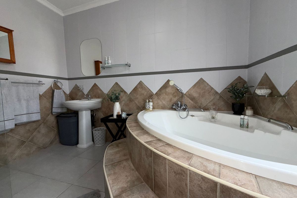 A functional bathroom featuring a corner bathtub with tiled surround and a pedestal basin, finished with neutral wall tiles.