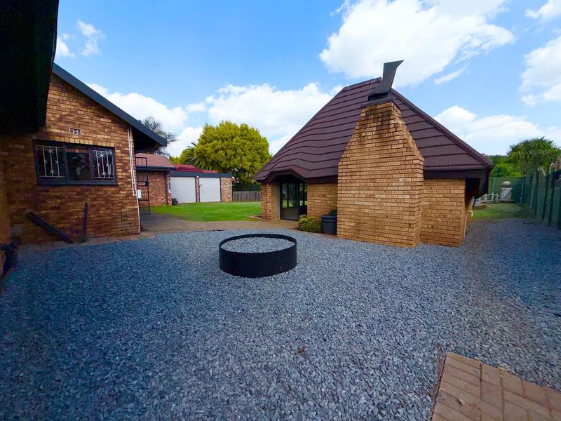 A rear exterior view featuring a brick house with a tiled roof, a gravel courtyard with a fire pit, and a detached garage.