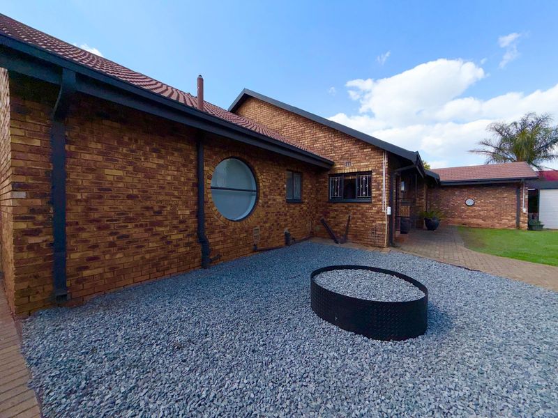Rear exterior view of a face brick house featuring a distinctive circular window, gravel landscaping, and a paved walkway.