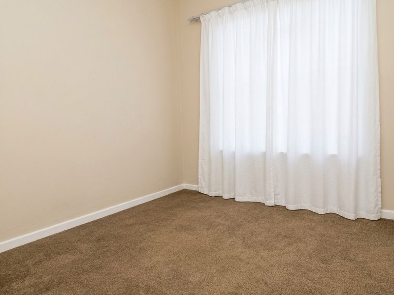 A clean, empty bedroom featuring neutral wall paint, brown carpeting, and a fitted curtain rail.